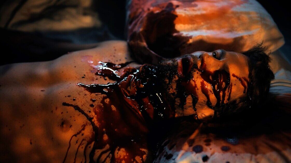 Josh's lifeless body bathed in red lighting in Thinestra (2026), a horror film about weight-loss drugs and bodily autonomy. Image courtesy of Breaking Glass Pictures.